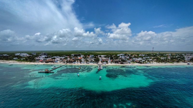 Puerto Morelos desde el aire: el pueblo bajo junto a la playa, los muelles, el faro y el arrecife bajo el agua.